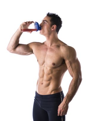 Muscular male bodybuilder drinking protein shake from blender